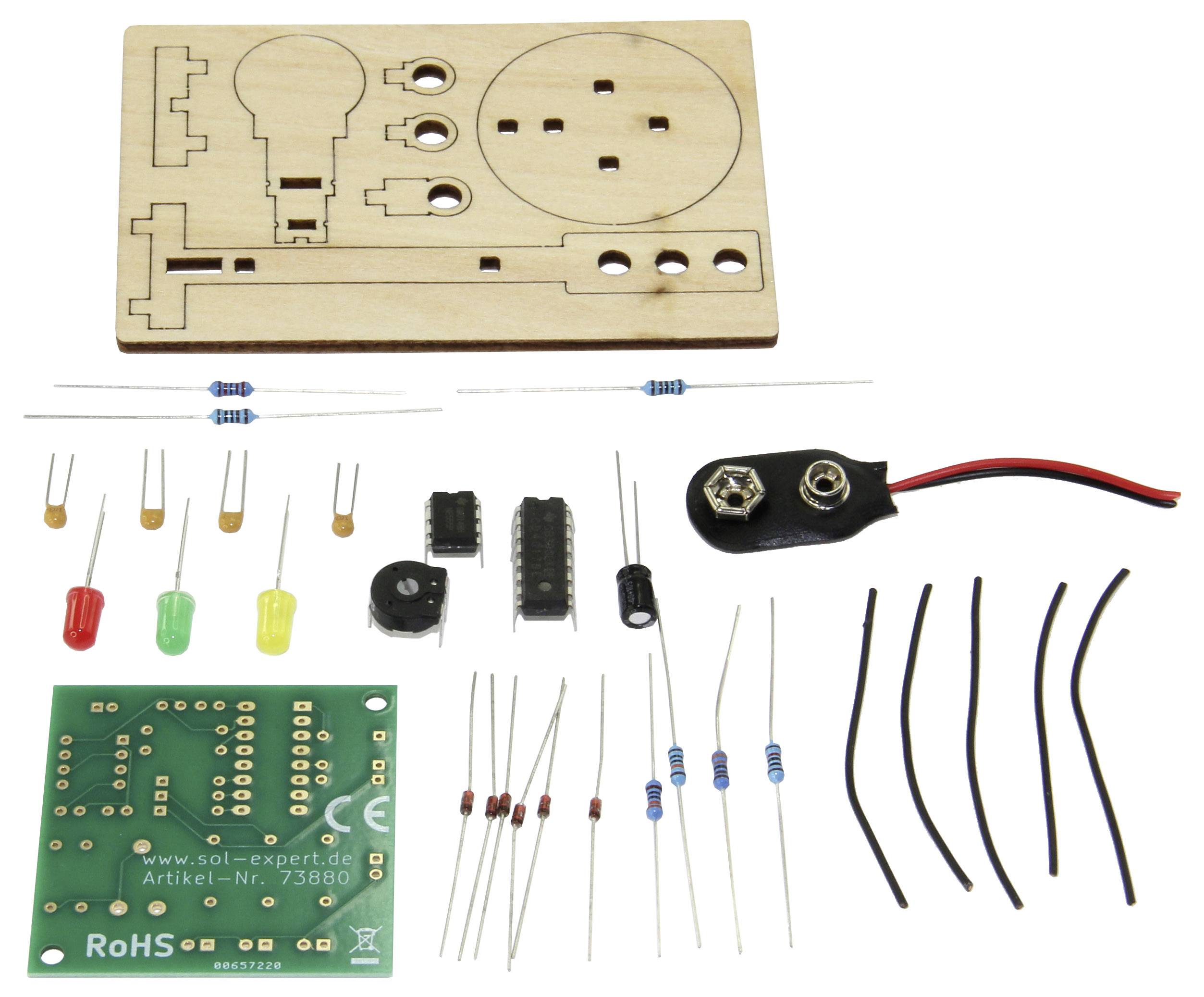 Elektronický stavebnicový kit s dřevěnými díly, různými rezistory, LED diodami, mikrokontrolerem, deskou plošných spojů a kabely. Obsahuje připojení pro baterii.