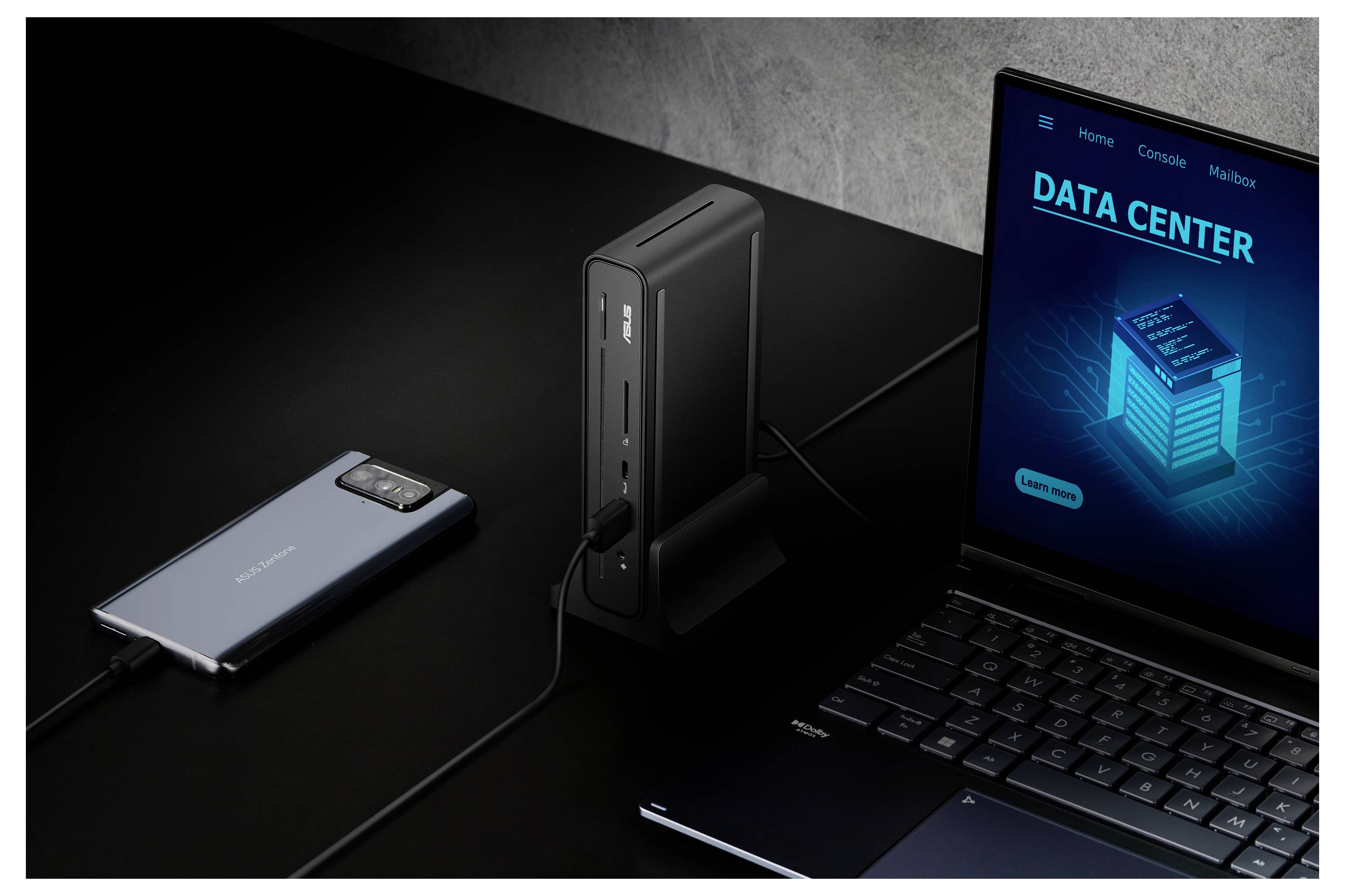 Chytrý telefon připojený k dokovací stanici vedle laptopů zobrazujícího 'DATA CENTER' na obrazovce, vše na tmavém povrchu.