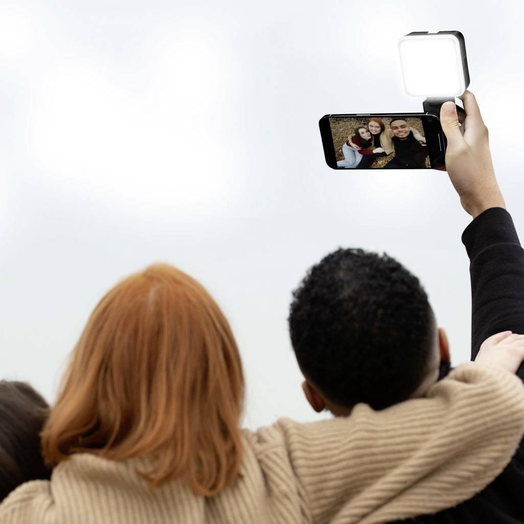 Tři lidé se objímají a s úsměvem si společně pořizují selfie venku na čerstvém vzduchu.