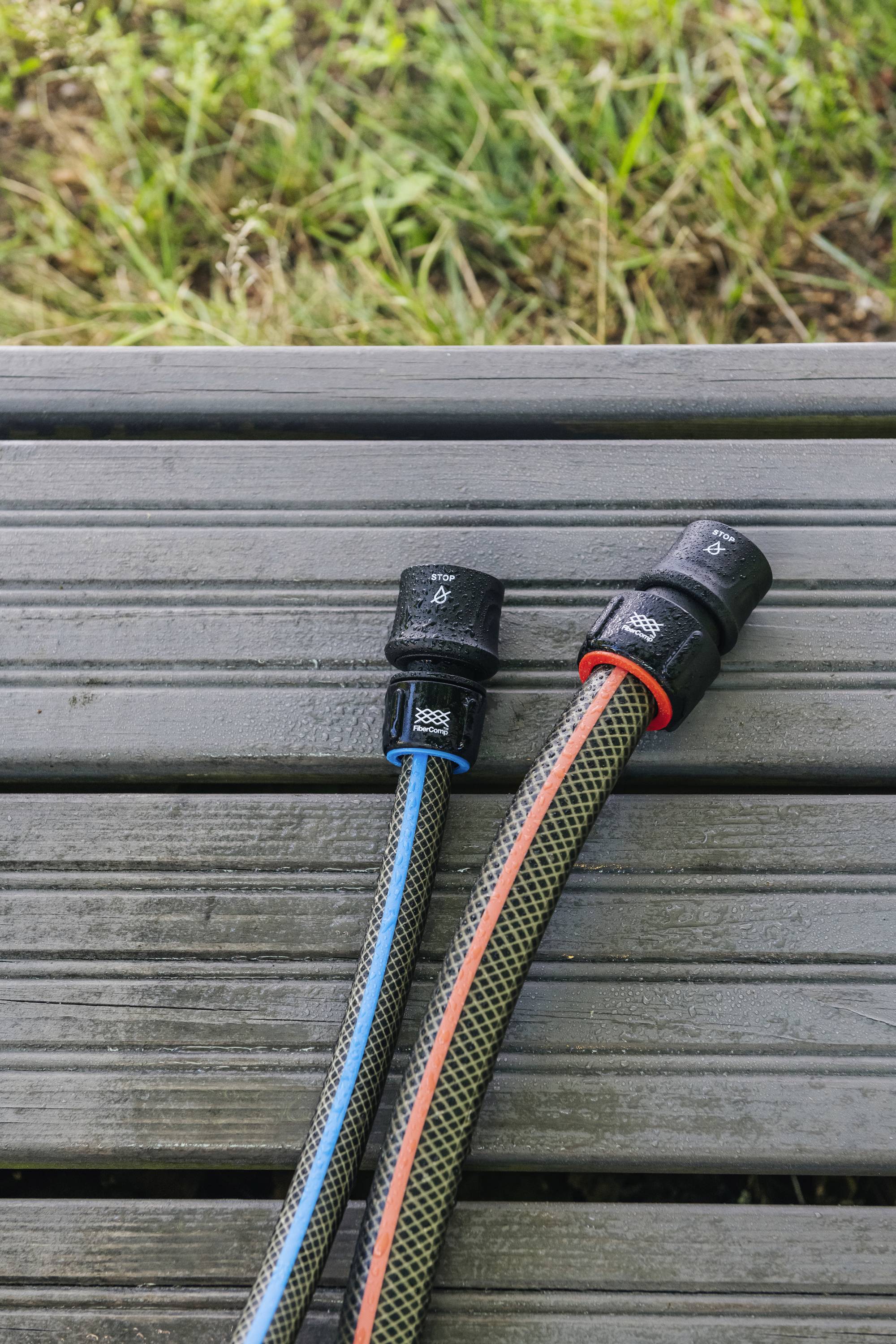Dva zahradní hadice s modrými a červenými pruhy na dřevěné terasové podlaze, obklopené zelenou trávou.