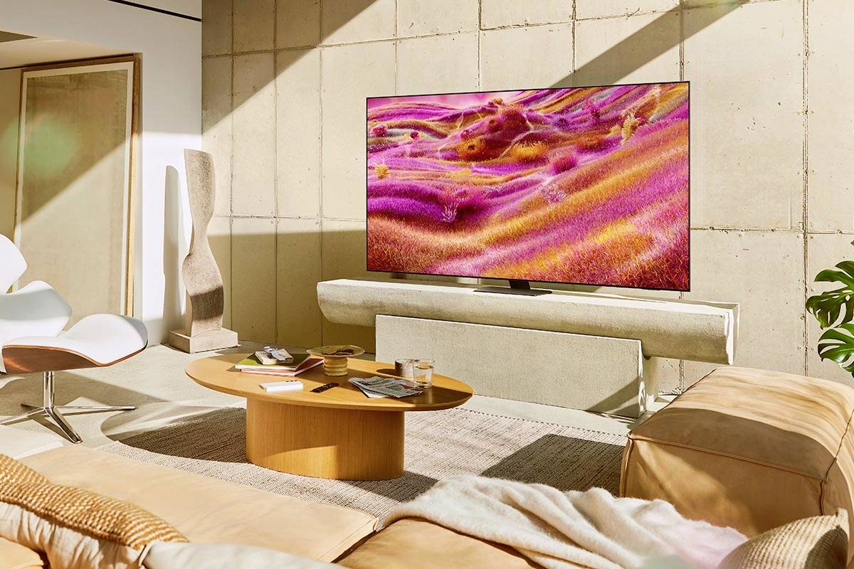Obývací pokoj s moderním designem: kožená pohovka, kulatý dřevěný stůl a velká plochá obrazovka na stěně. Světlé, teplé osvětlení.