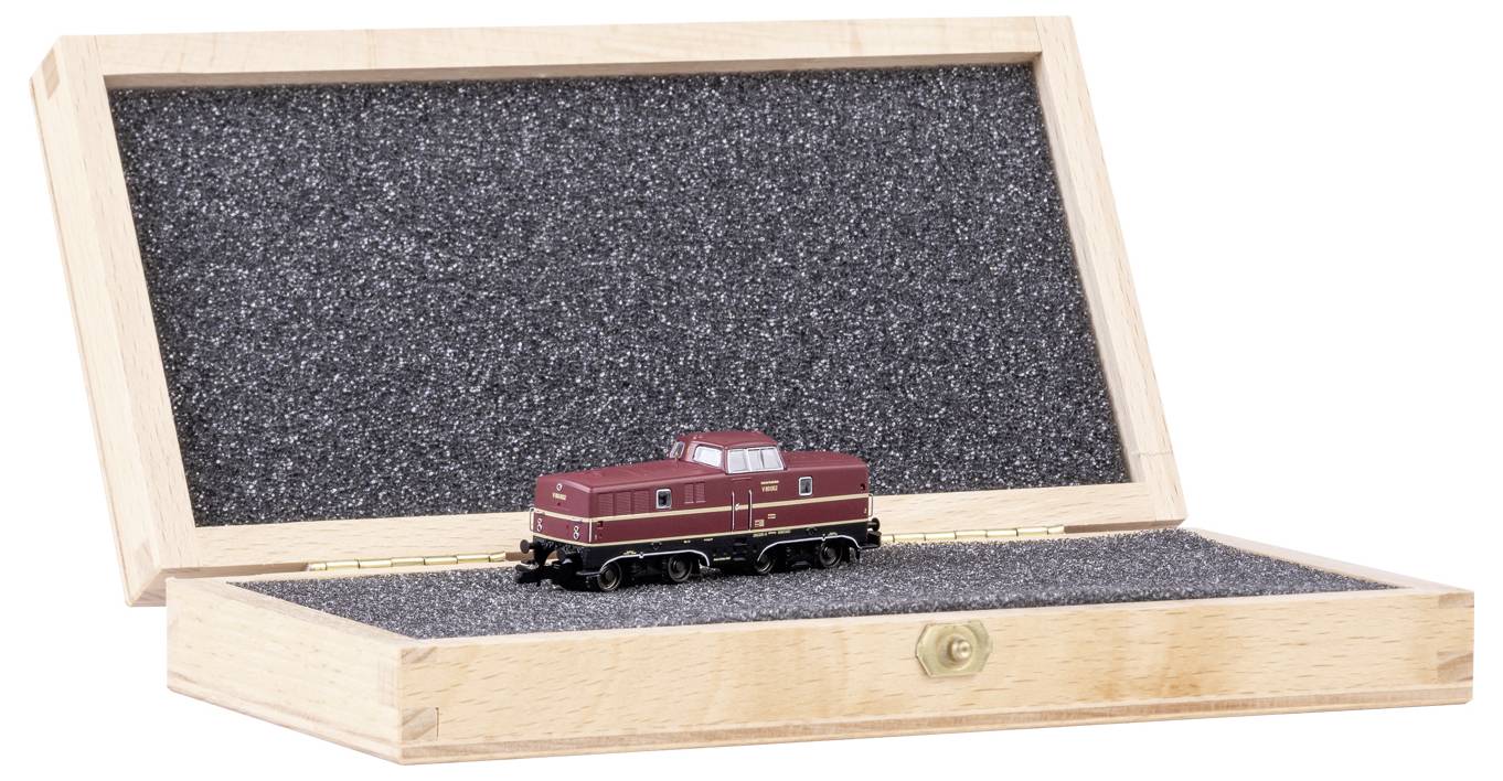 Malá modelová lokomotiva v otevřené dřevěné krabici vyložené černou pěnovou výplní. Lokomotiva je tmavě červená a precizně zpracovaná.
