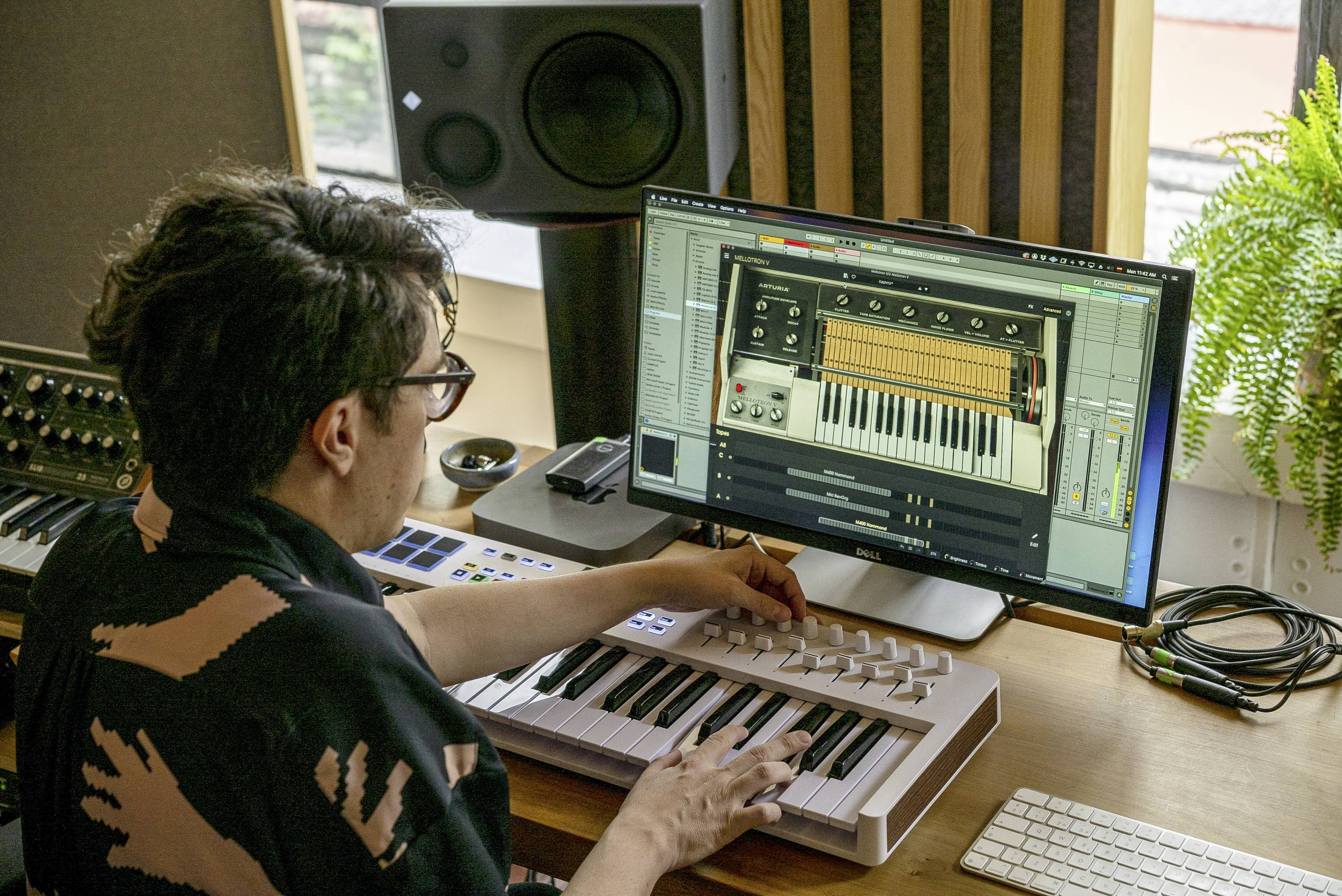 Osoba hraje na MIDI klávesách v hudebním studiu, zatímco používá hudební software na obrazovce počítače.