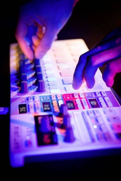 Ruce ovládají osvětlený DJ mixážní pult s různými tlačítky a posuvnými regulátory v tmavém prostředí.