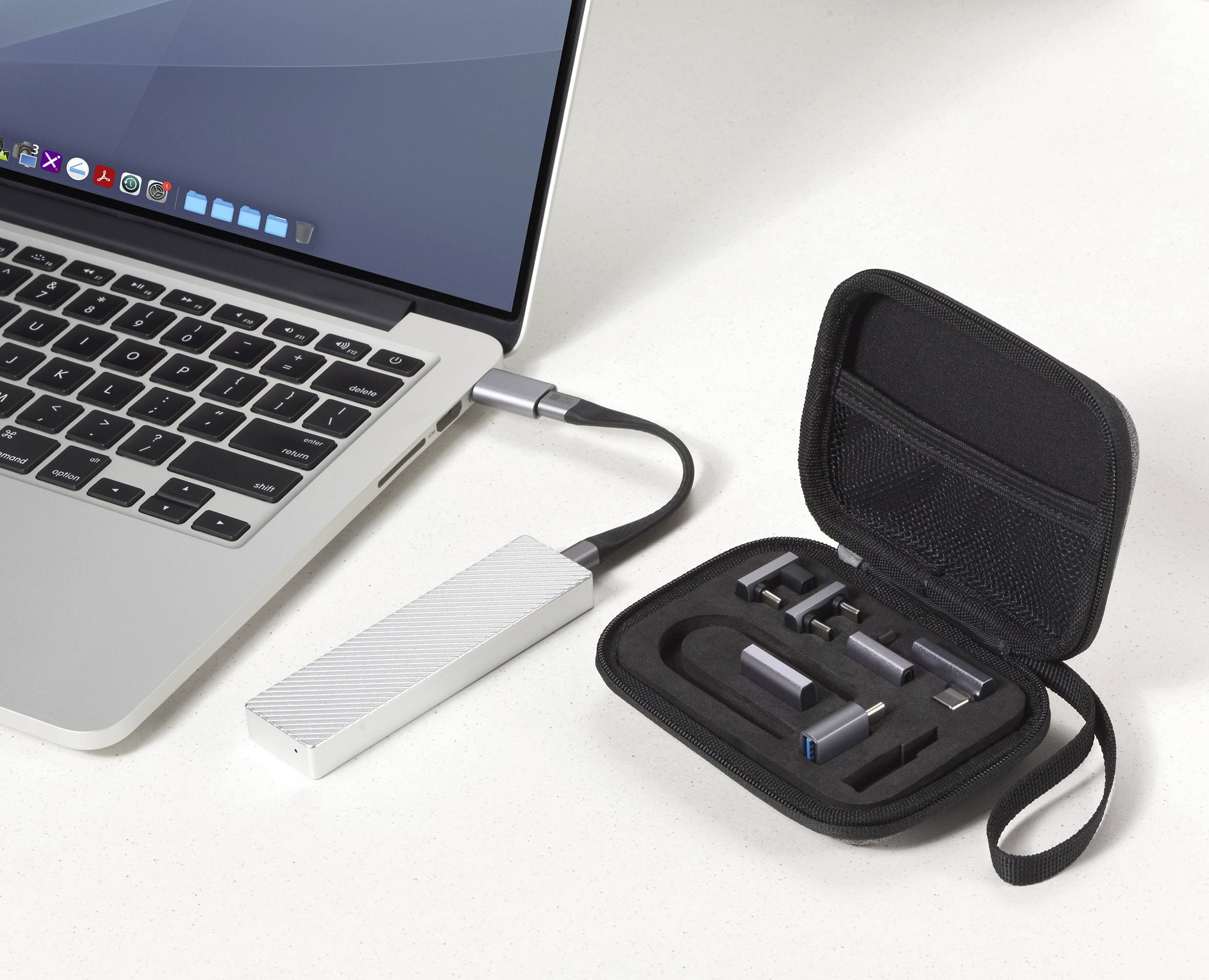 Laptop na stole je připojen k přenosnému externímu SSD disku. Vedle něj otevřený kryt zobrazuje několik USB konektorů a adaptérů.