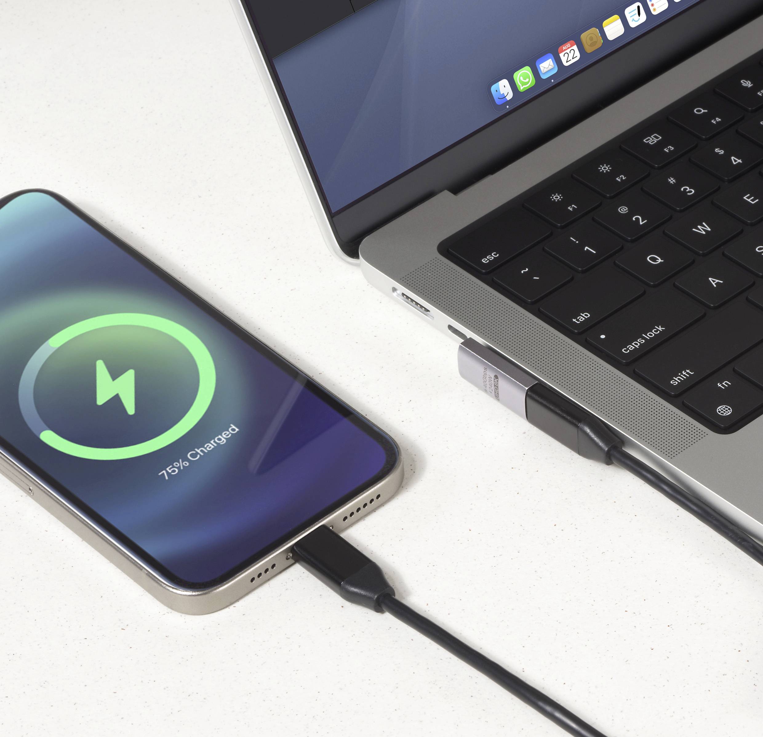 Chytrý telefon s nápisem „75% nabito" na obrazovce se bezdrátově nabíjí na nabíjecí podložce. Vedle něj leží laptop s připojeným USB zařízením na stole.