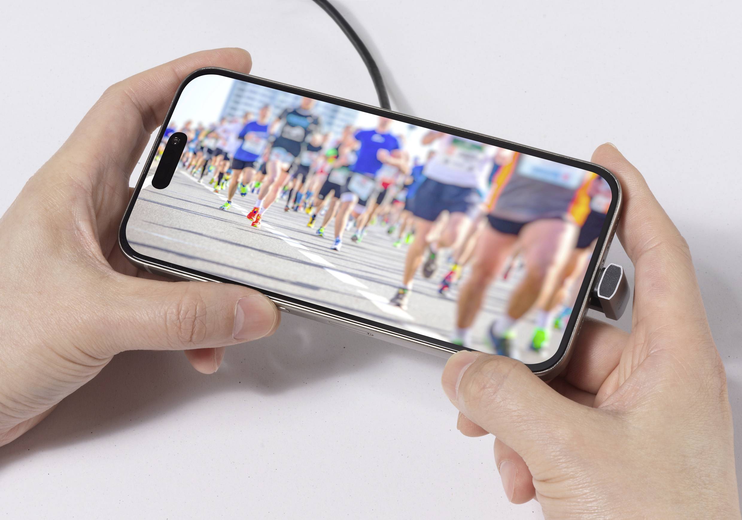 Ruce držící telefon zobrazující rozmazaný obraz běžců v maratonu, zaměřený na pohyb davu a rozmanitost běžeckého vybavení.