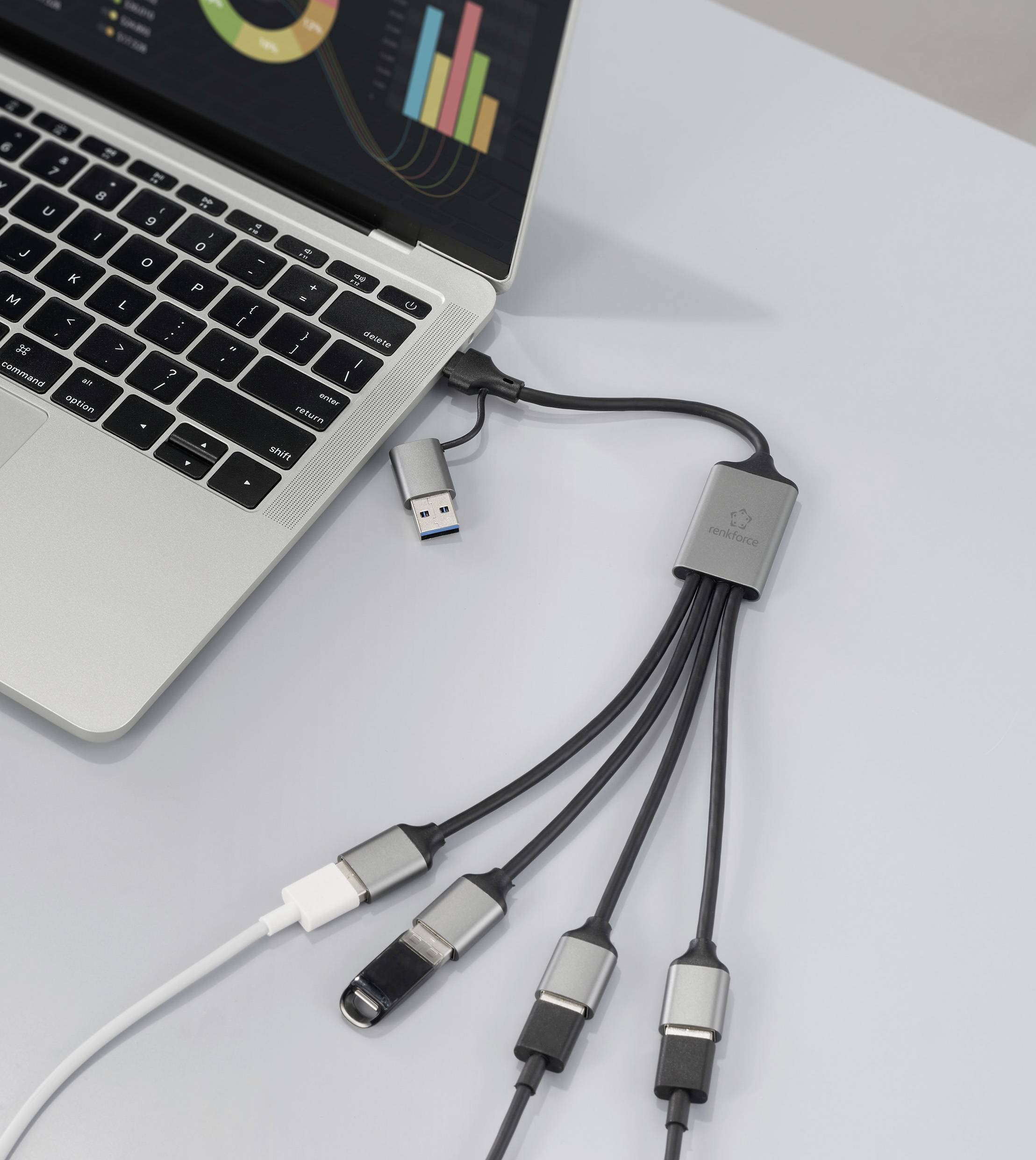Laptop připojený k USB rozbočovači s více porty, na jehož obrazovce je zobrazen barevný datový graf. Do rozbočovače jsou zapojeny různá zařízení.