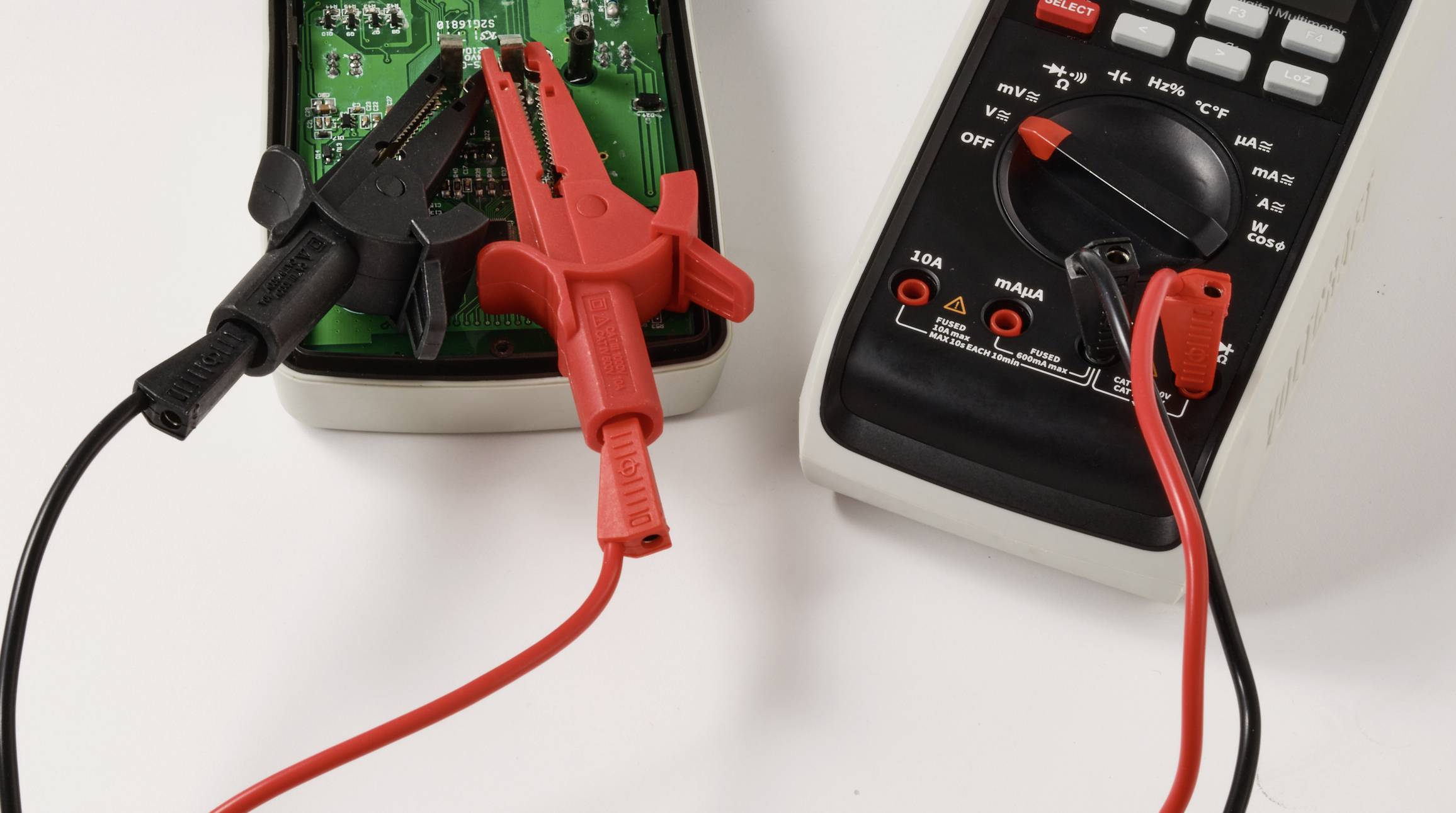 Digitální multimetr s červenými a černými měřicími sondami je připojen k zelené desce plošných spojů a měří elektrické hodnoty.