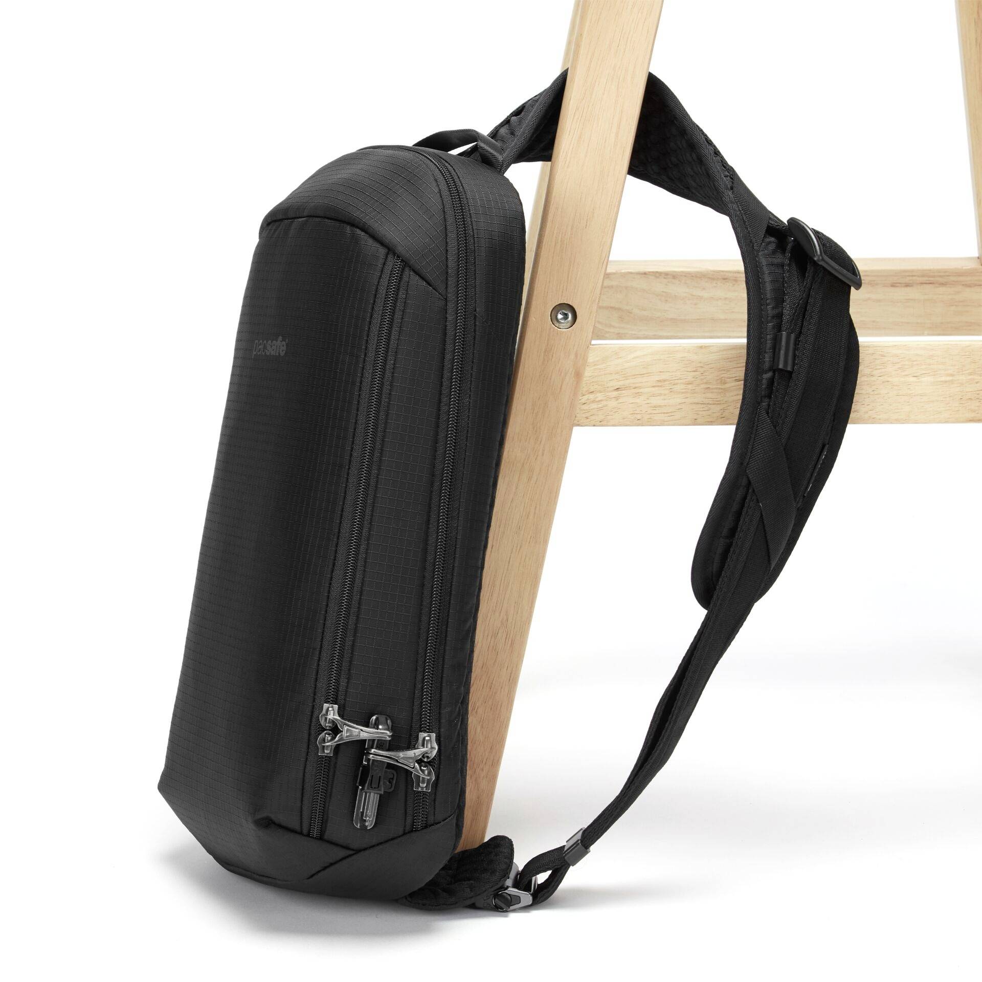 Černý batoh visí na dřevěné židli, disponuje několika zipy a elegantním designem, který odkazuje na moderní a praktický styl.