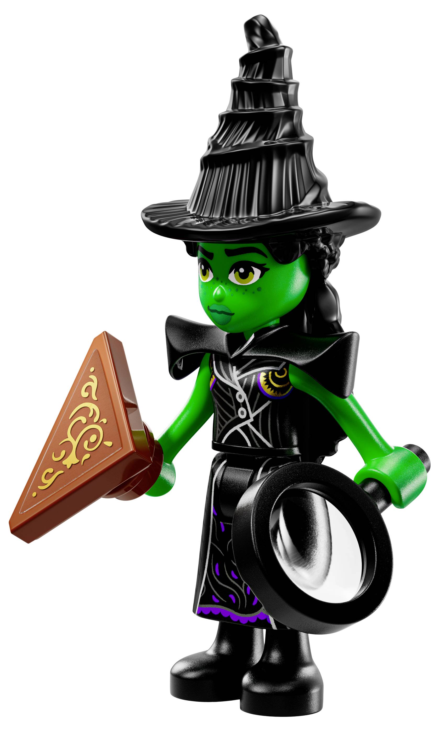 Figurka LEGO čarodějnice se zeleným obličejem, vysokým černým kloboukem, která drží trojúhelníkový plát čokolády a kulatou zvětšovací lupu.