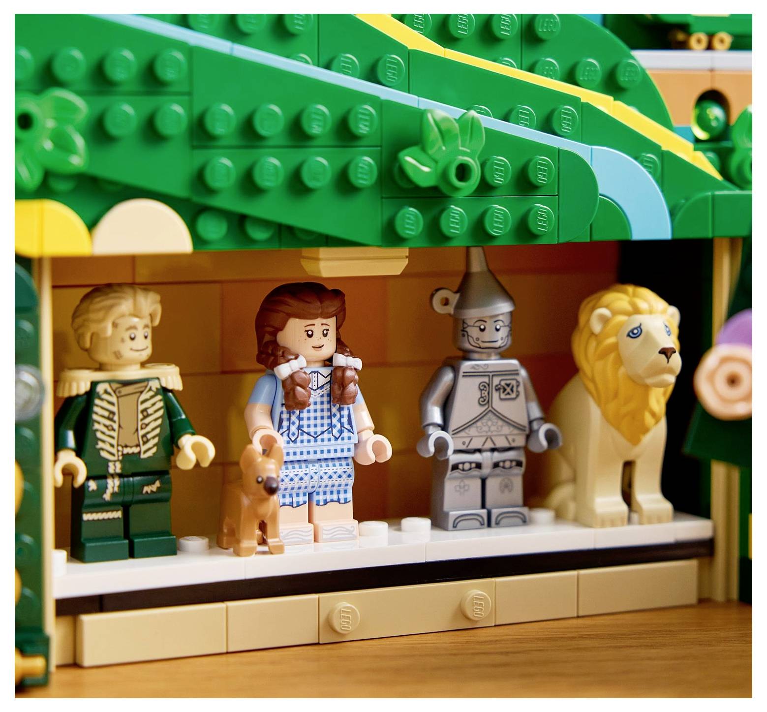 Lego figurky znázorňující postavy z filmu 'Čaroděj ze země Oz': Strašák, Dorothy se psem Totošem, Plecháč a Zbabělý lev, na pódiu.