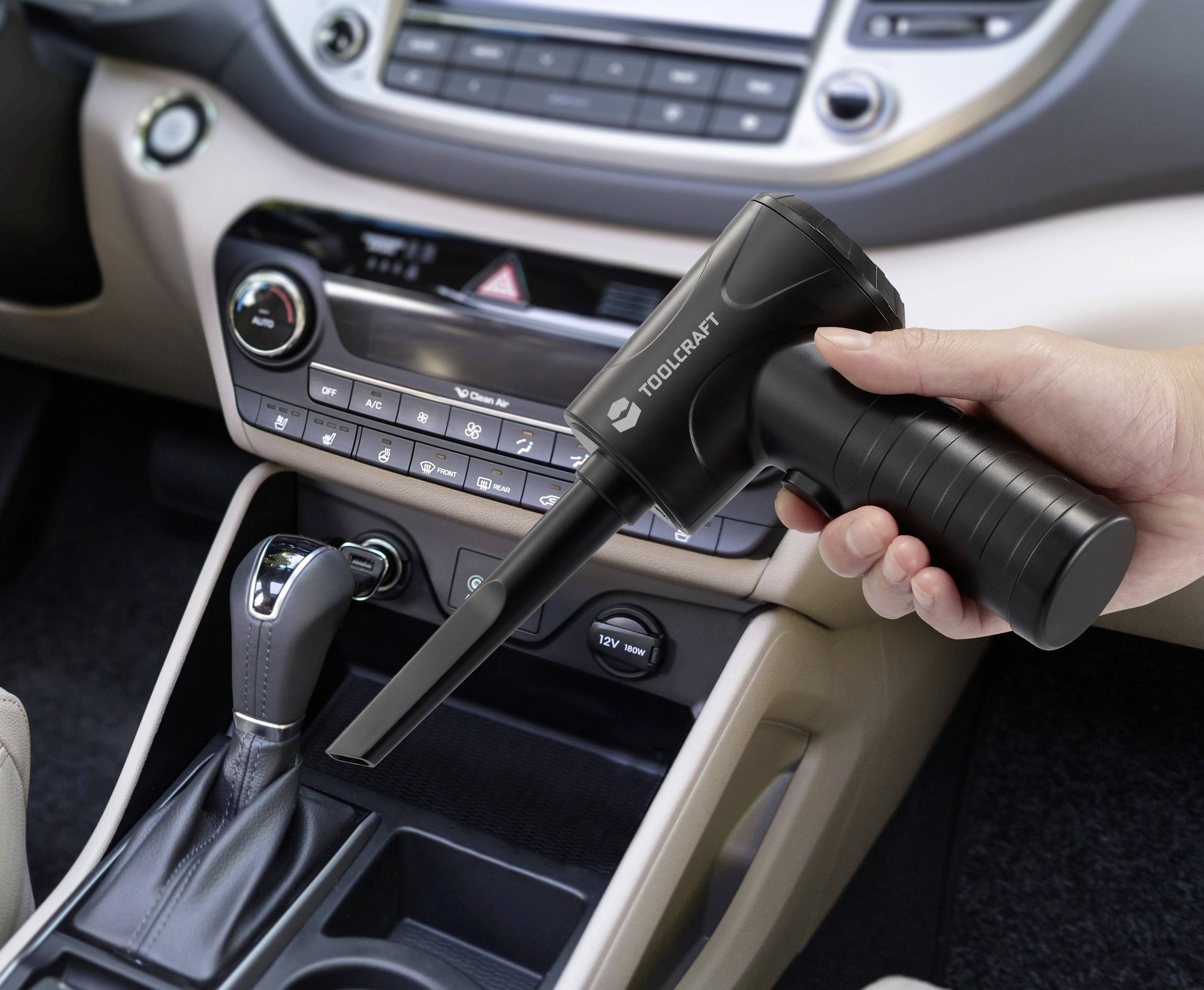 Ruka držící kompaktní černý stlačený vzduch v interiéru automobilu, namířený do oblasti řadicí páky pro čištění nečistot.