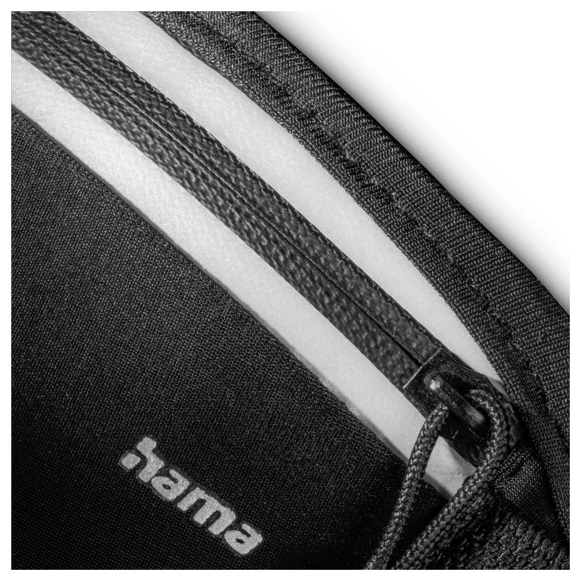 Detailní záběr černobílého zipu na látce s textem 'hama'.