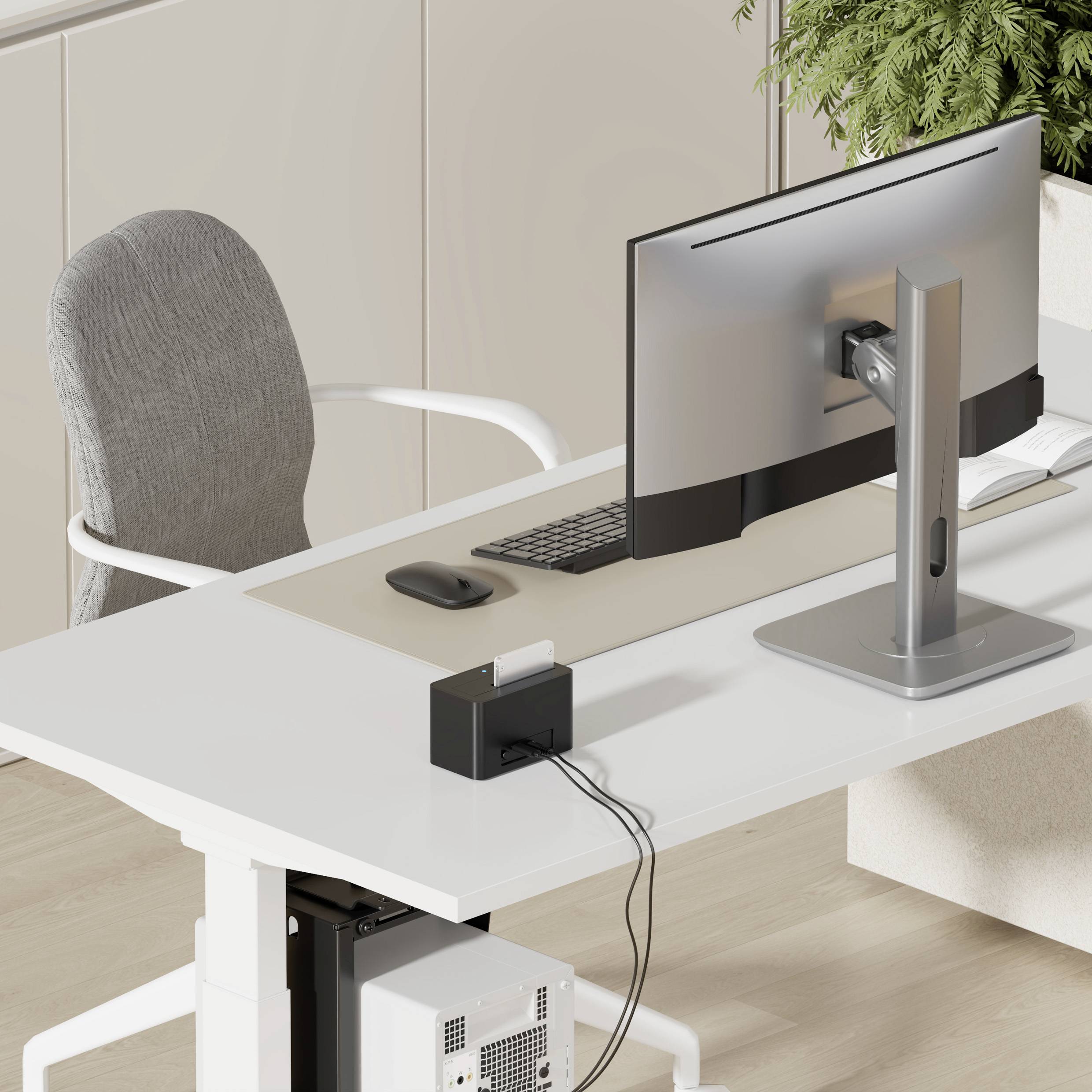 Moderní, minimalistická domácí kancelář s velkým monitorem na bílém stole, židlí a pokojovou rostlinou v rohu.