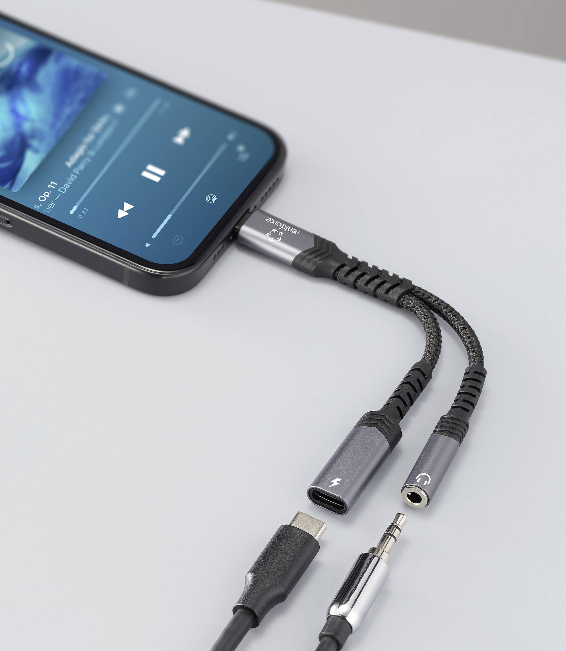 Smartphone přehrávající hudbu je připojen k duálnímu adaptéru s konektory USB-C a 3,5mm jackem na stole.