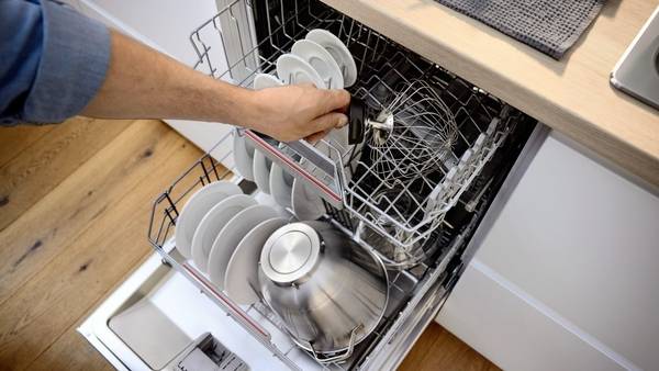Osoba vkládá nádobí a kuchyňské vybavení do otevřené myčky v kuchyni a ukazuje efektivní umístění nádobí pro optimální mytí.