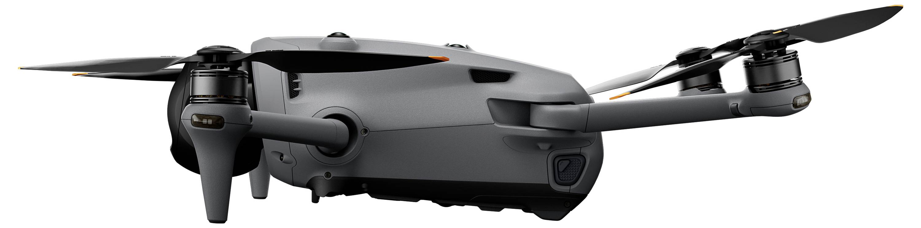 Kompaktní šedý dron se čtyřmi roztaženými vrtulemi, pohled z boku. Dron má elegantní design a nachází se na bílém pozadí.