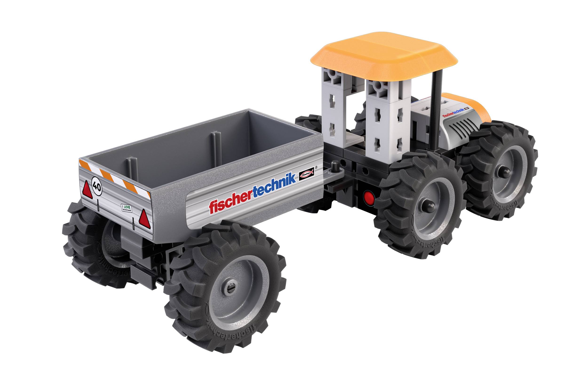 Hračkářský traktor s přívěsem, na jehož boku je vyznačeno logo 'fischertechnik', má velká černá kola a žlutou střechu.
