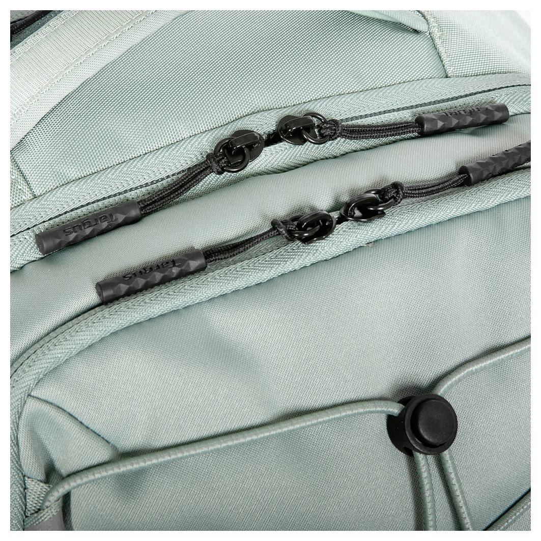Detailní záběr zipů a popruhu na světle zelené tašce, zachycující detaily látky a designových prvků.