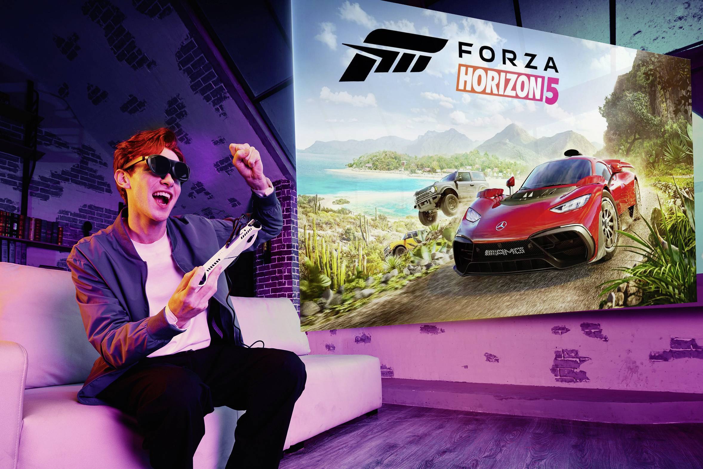 Osoba sedí nadšeně na gauči, drží herní ovladač, přičemž na obrazovce je zobrazena hra 'Forza Horizon 5' s auty v pestré krajině.