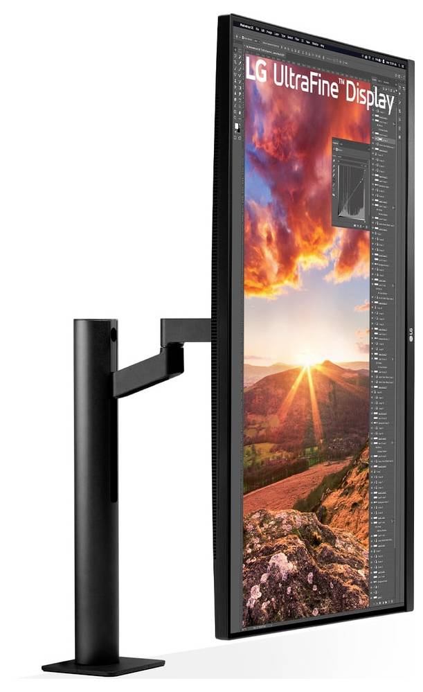 Vertikálně orientovaný monitor LG UltraFine Display zobrazující živé krajinné scenérie se zapadajícím sluncem nad kopci, umístěný na černém stojanu.