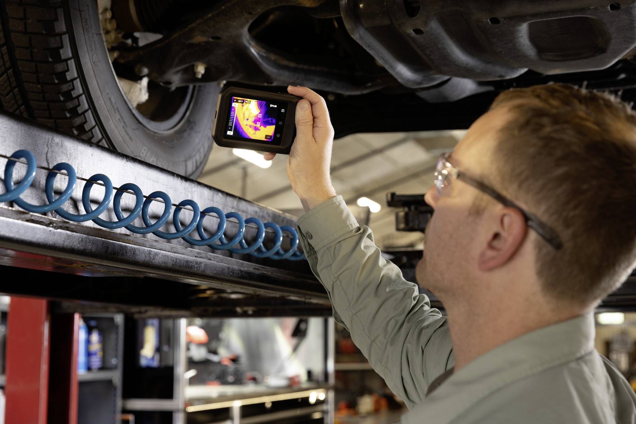 Mechanik kontroluje spodní část vozidla termovizní kamerou a zvýrazňuje teplotní rozdíly v autoservisu.