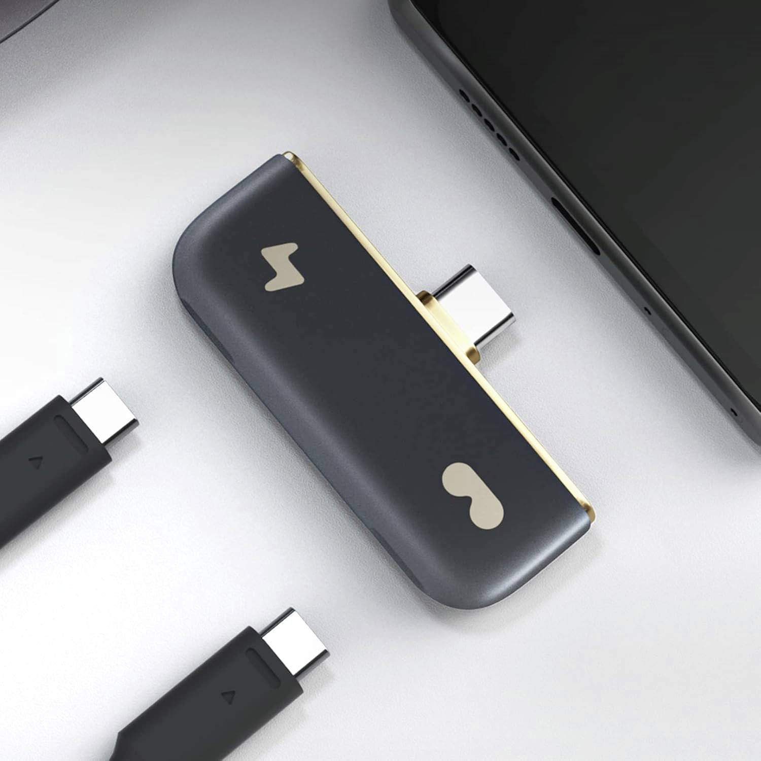 Rozbočovač USB-C s dvěma porty připojený k chytrému telefonu, s dalšími kabely USB-C v okolí.