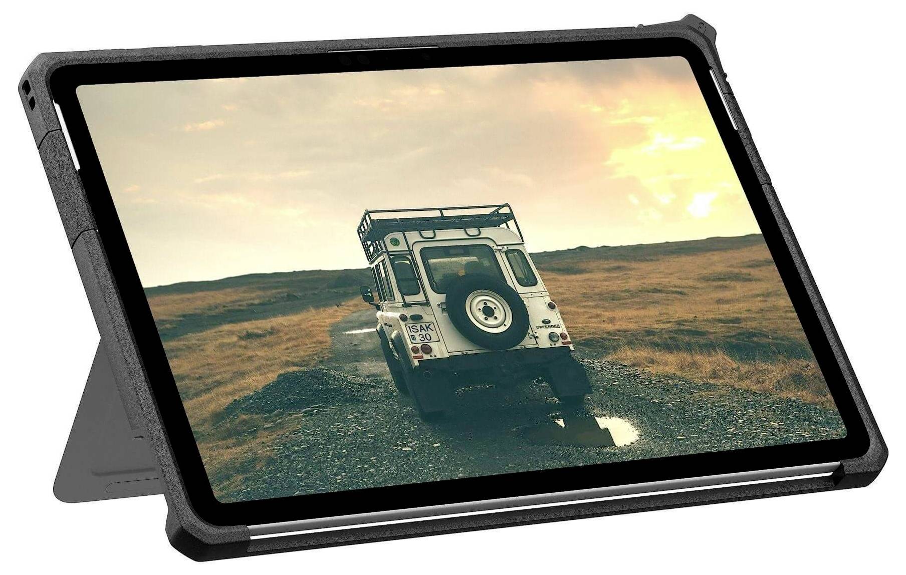 Tablet zobrazující obraz bílého terénního vozidla na štěrkové cestě, s pozadím zapadajícího slunce nad pustou krajinou.