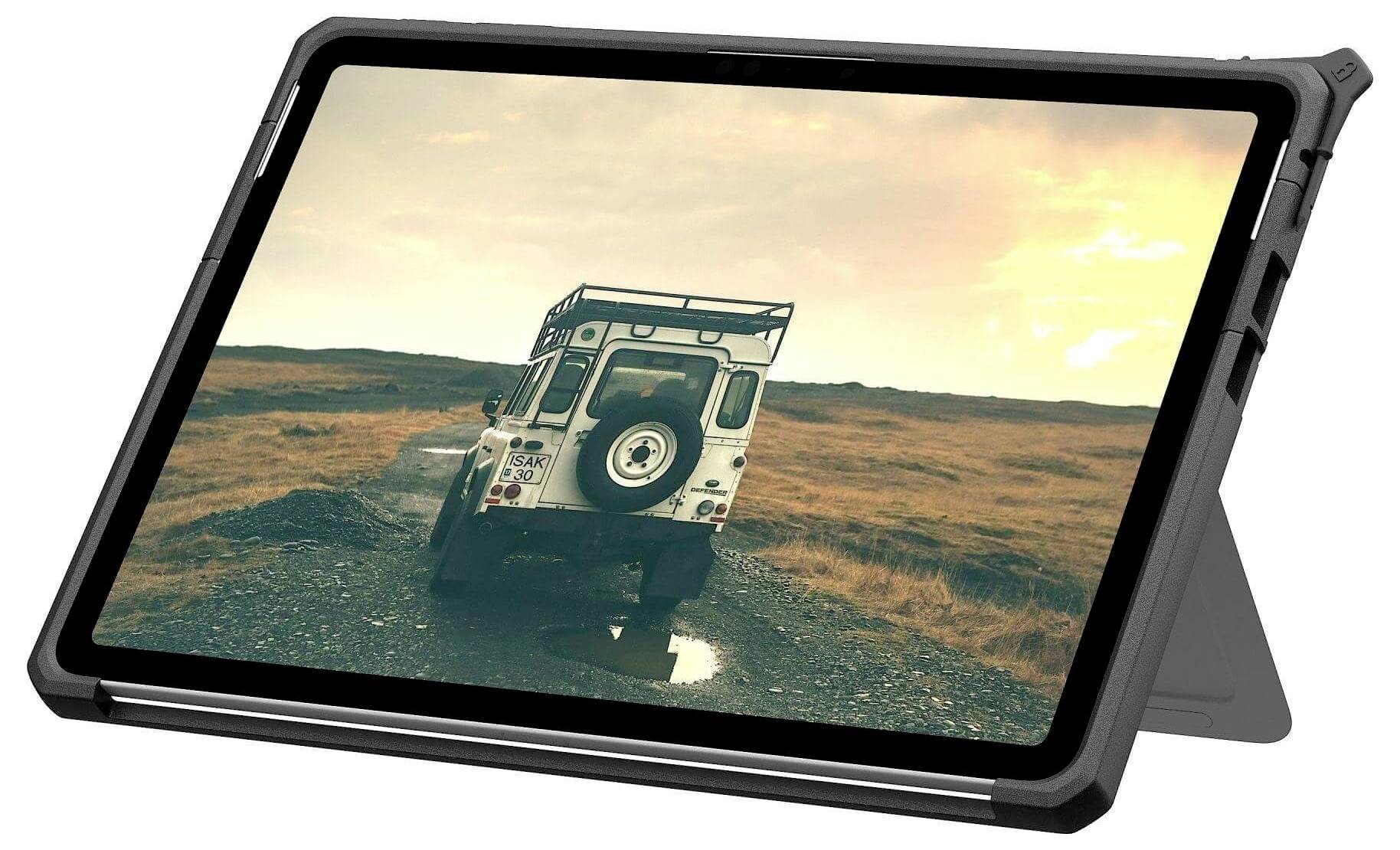 Tablet zobrazující obraz robustního vozidla na štěrkové cestě procházející puskatou krajinou za soumraku. Scéna navozuje atmosféru dobrodružství a průzkumu.