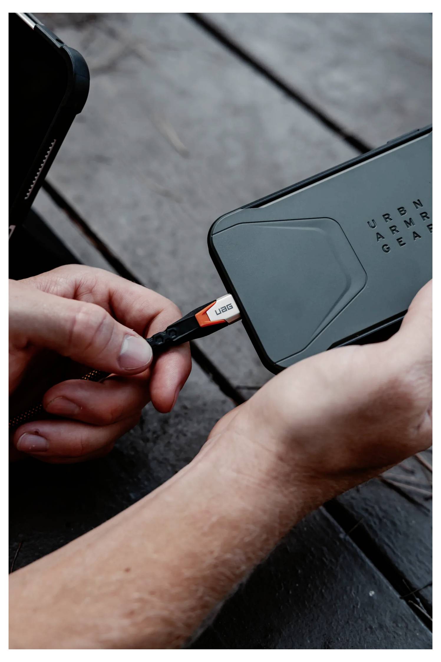 Osoba zapojuje nabíjecí USB kabel do smartphonu na dřevěném povrchu.