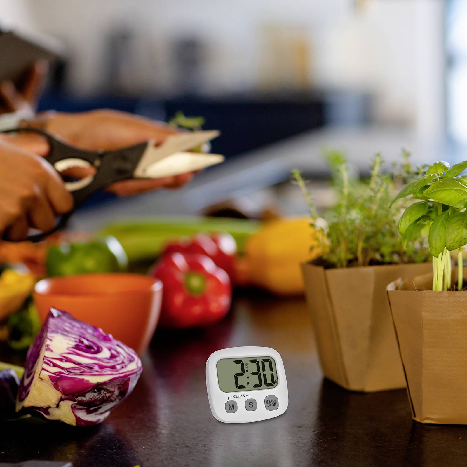 Osoba krájí zeleninu v kuchyni, přičemž digitální timer ukazuje '2:30'. Na pracovní ploše jsou viditelné čerstvé potraviny včetně paprik a bazalky.