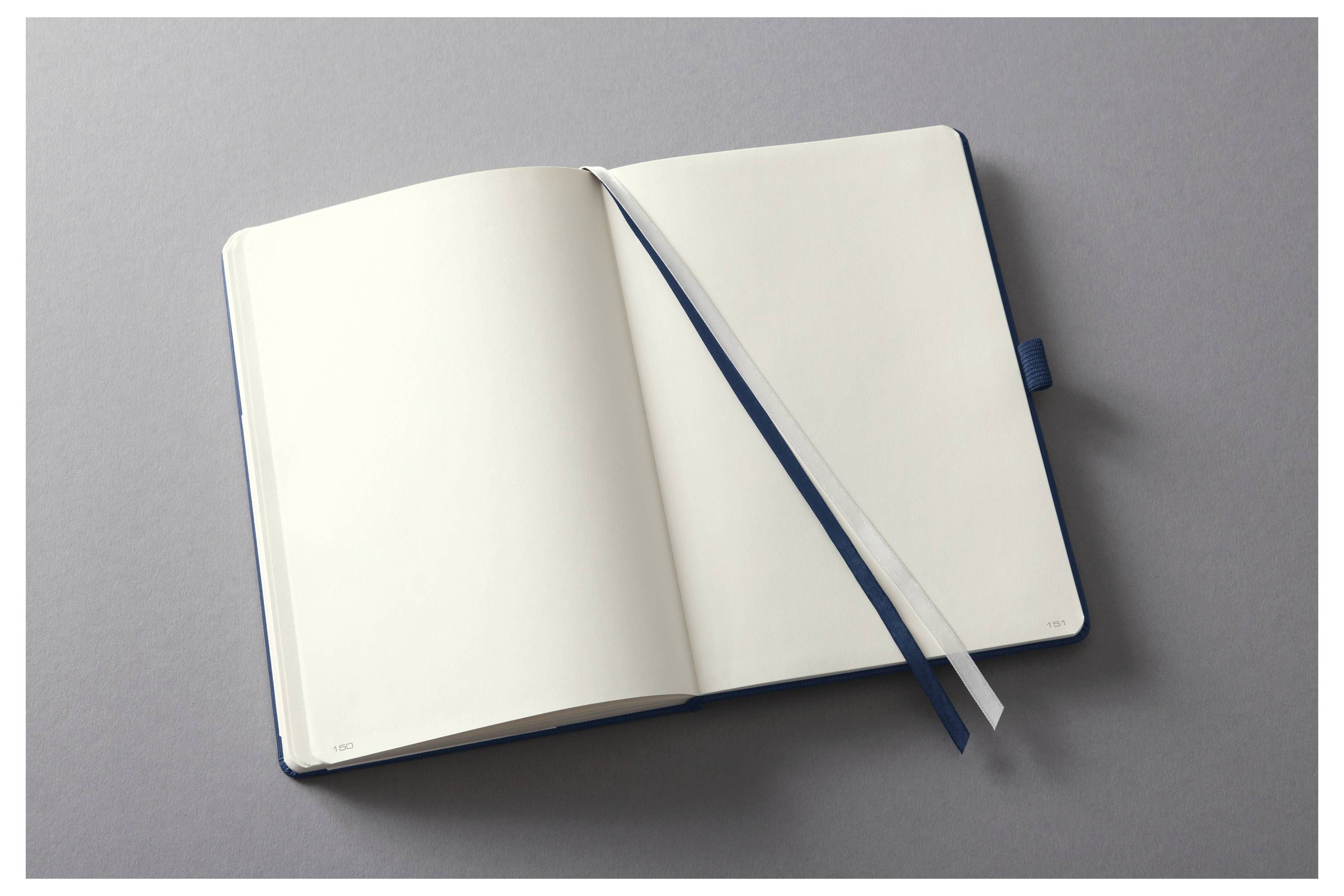 Otevřený notes s prázdnými bílými stránkami a bílou stužkou jako záložkou leží na šedém povrchu, připravený na psaní nebo kreslení.