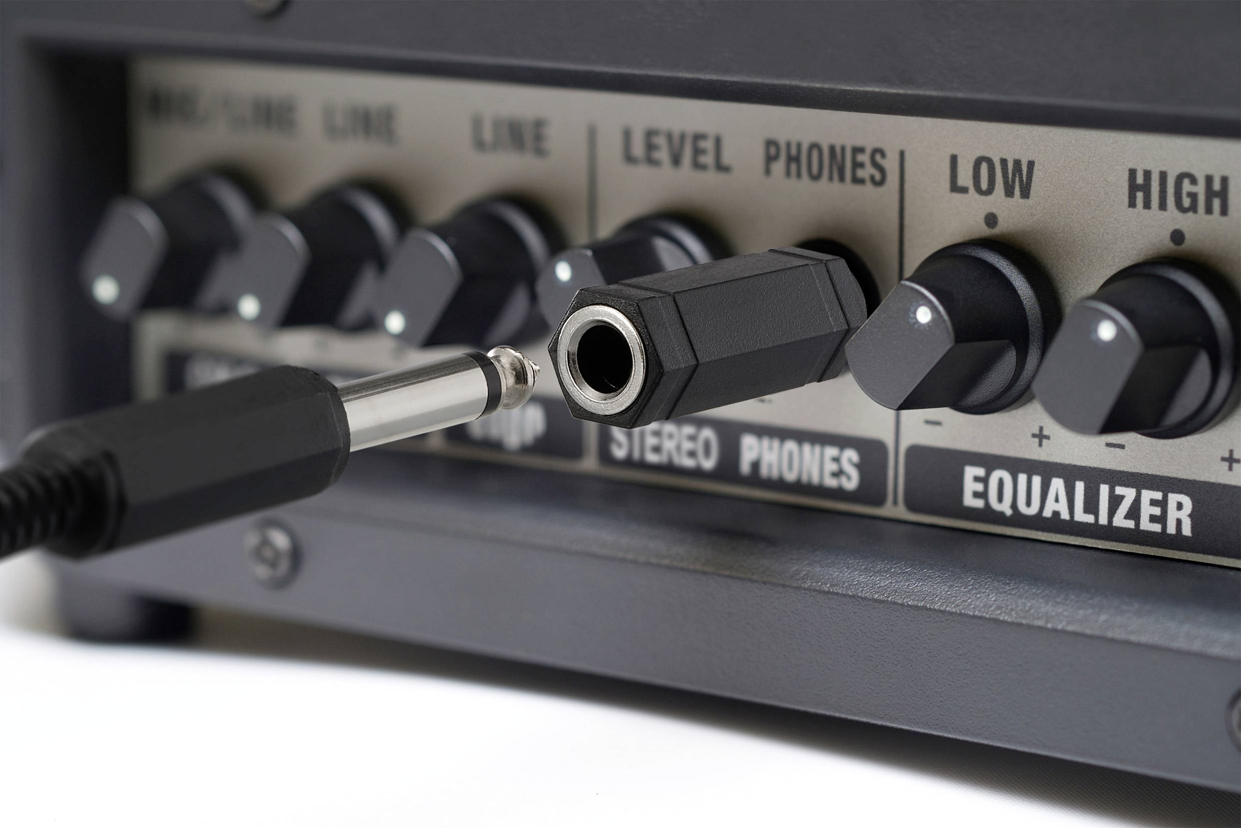 Detailní záběr audiotechniky ukazuje několik knoflíků a nevložený audio konektor. Štítky obsahují nápisy „Úroveň", „Sluchátka" a „Ekvalizér".