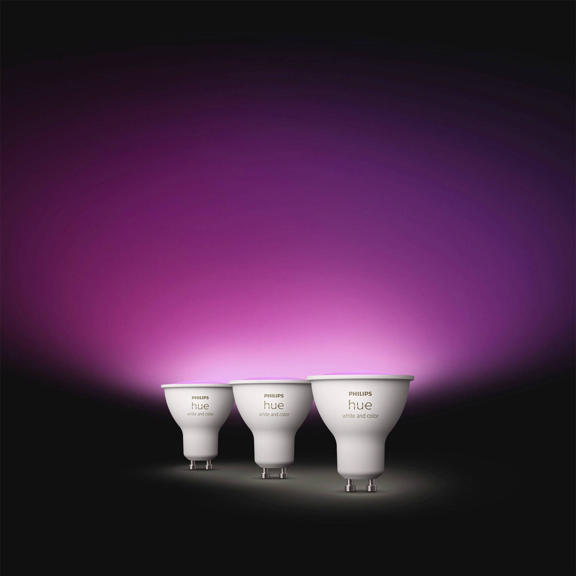 Tři chytré žárovky Philips Hue jsou vystaveny na fialovém osvětleném pozadí, které zvýrazňuje jejich schopnost měnit barvu osvětlení.