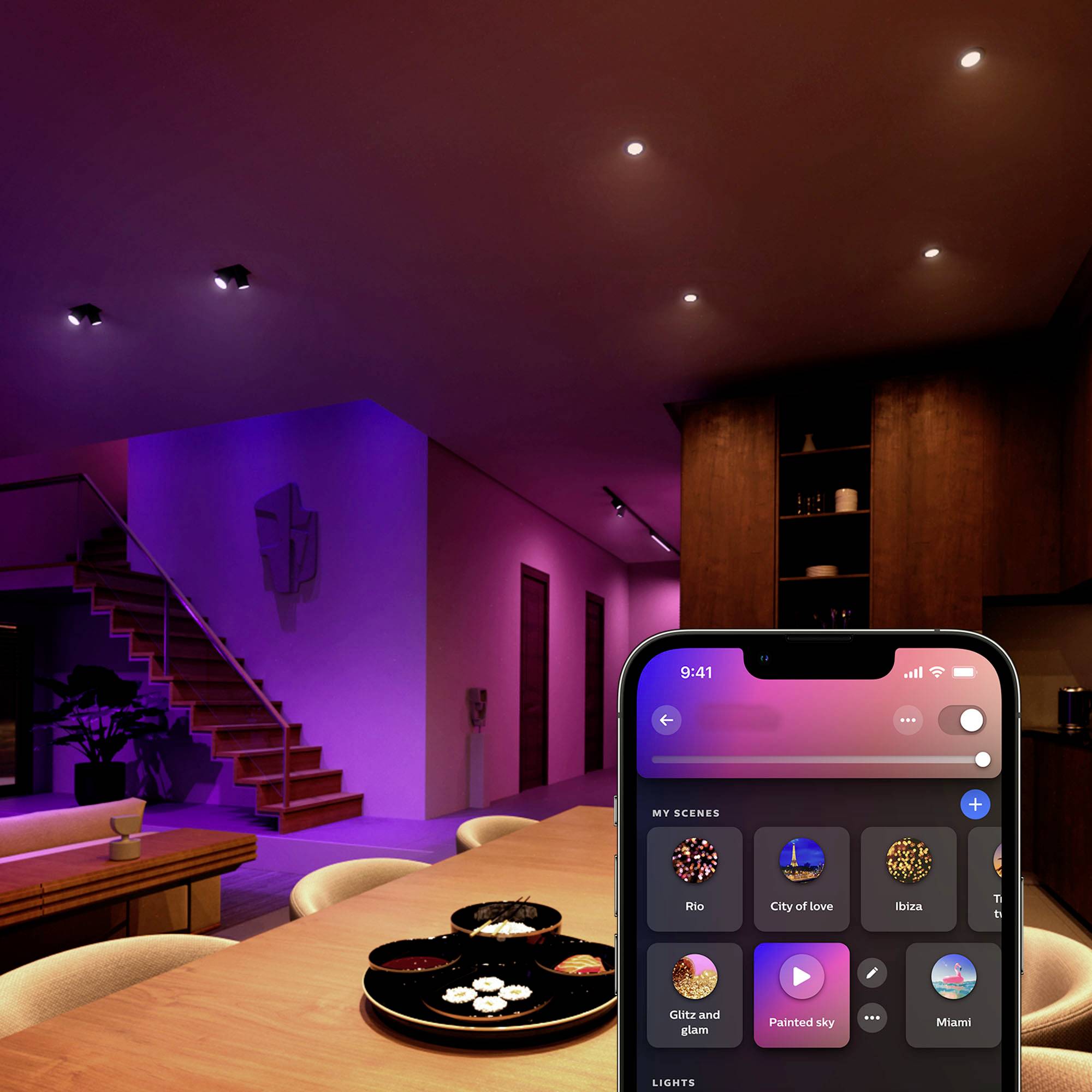 Moderní obývací pokoj s fialovým ambientním osvětlením. Smartphone zobrazuje rozhraní aplikace pro chytré osvětlení s výběrem scén, jako je například „Město lásky".