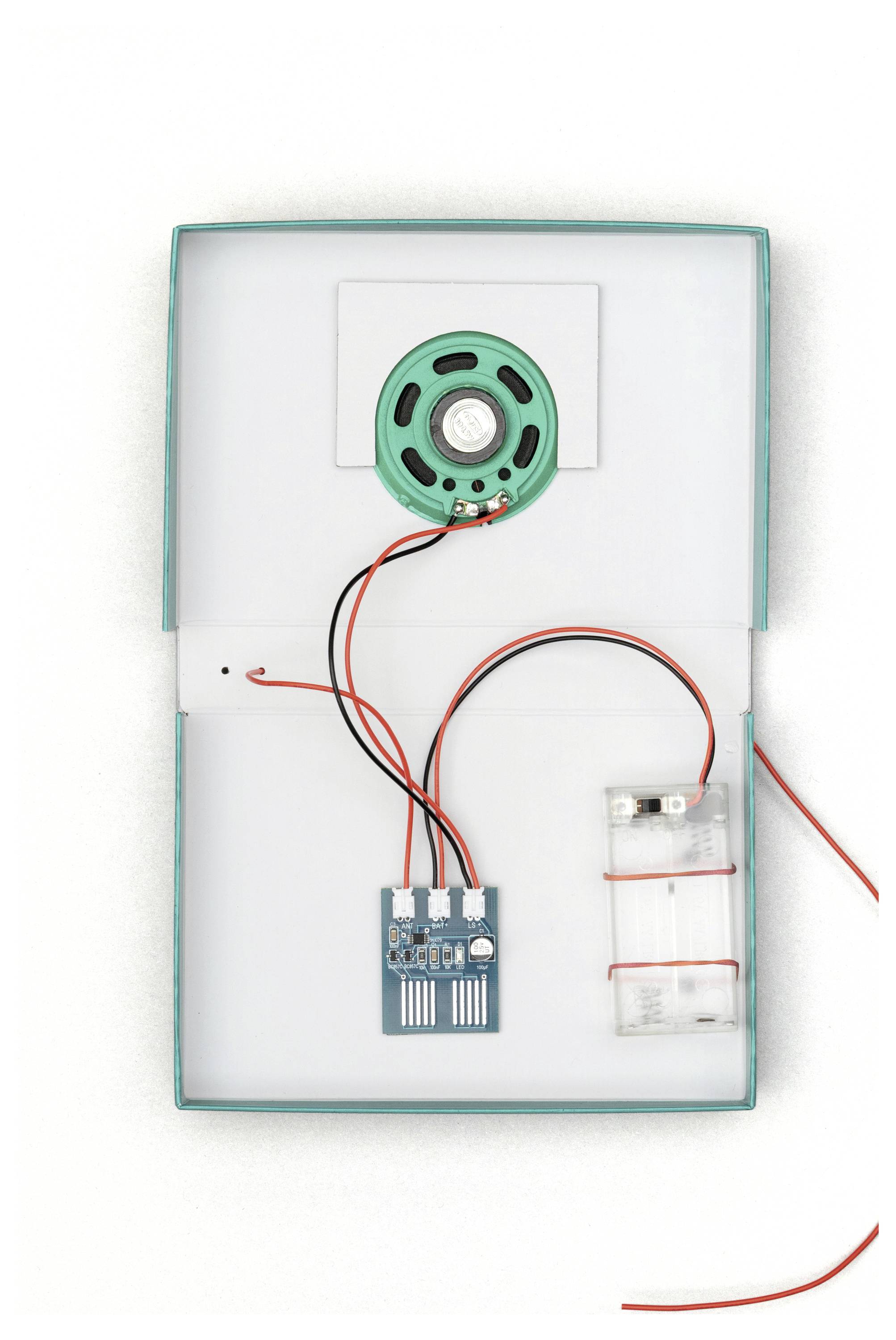 Otevřená elektronická projektová krabice s reproduktorem, deskou plošných spojů a držákem baterie uvnitř, propojené červenými a černými vodiči.