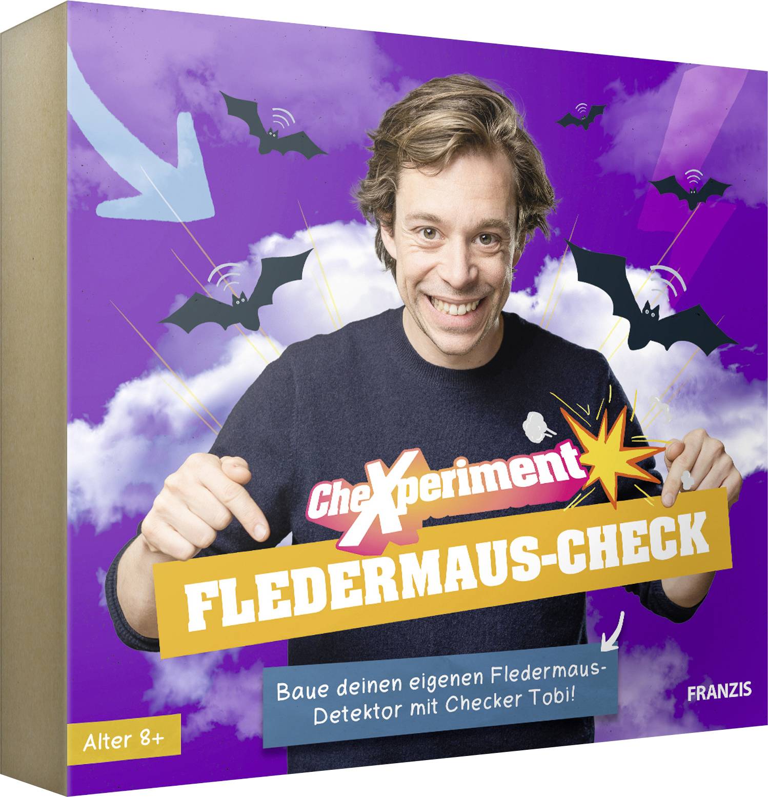 Usmívající se osoba ukazuje na krabici vědecké sady s motivem netopýra s názvem „FLEDERMAUS-CHECK", což naznačuje, že je vhodná pro děti od 8 let.