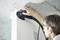 Osoba v ochranných brýlích používá elektrické nářadí s připojenou zelenou hadicí, aby vyhladila hranu stěny pod betonovým stropem.
