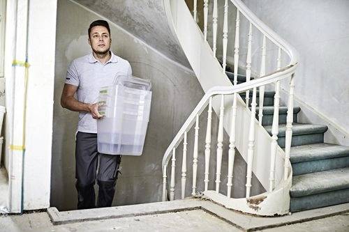 Osoba nesoucí velkou průhlednou úložnou nádobu po zakřiveném schodišti v budově, která je v rekonstrukci.