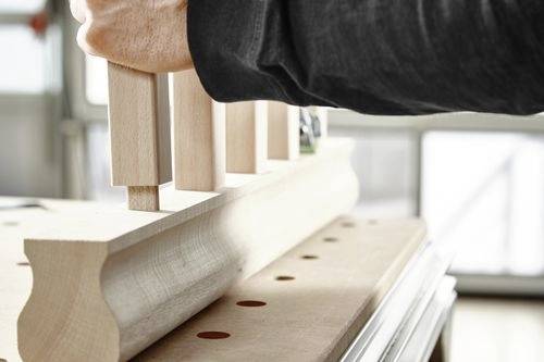 Osoba montující dřevěné komponenty, zasazující obdélníkové díly do drážkované základny na pracovním stole, předvádějící řemeslné dovednosti.