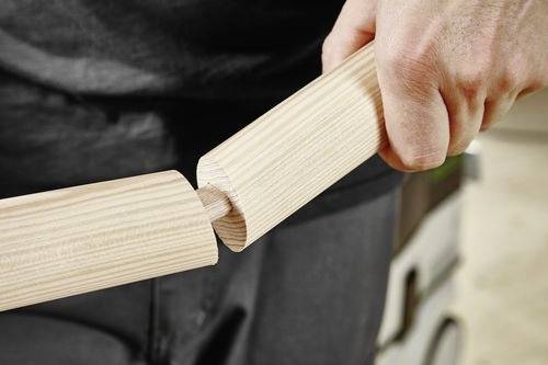 Osoba předvádějící tesařský spoj, ukazující dvě dřevěné části přesně do sebe zapadající.