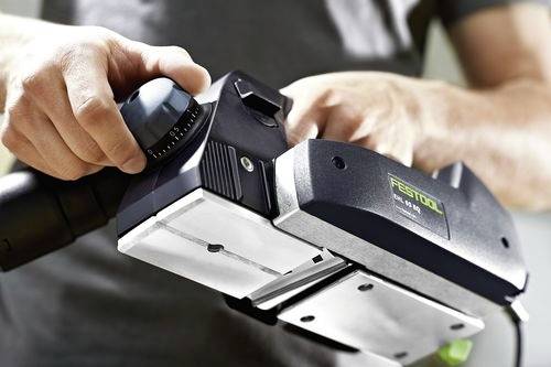 Osoba nastavující ruční elektrický nástroj, soustředěná na otočný knoflík s měřítkem. Nástroj vypadá, že je nastaven pro přesné použití na projektu.