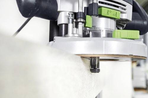 Detailní záběr elektrické frézky vyhlazující hranu dřevěné desky, s viditelnými seřizovacími otočnými knoflíky a řezným nástrojem.