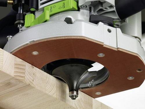 Detailní snímek elektrické frézky, která řeže hranu dřevěné desky. Fréza má zelený a stříbrný kryt.