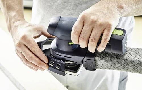 Osoba používá ruční elektrickou brusku na dřevěném povrchu, zaměřuje se na vyhlazení a konečnou úpravu materiálu.