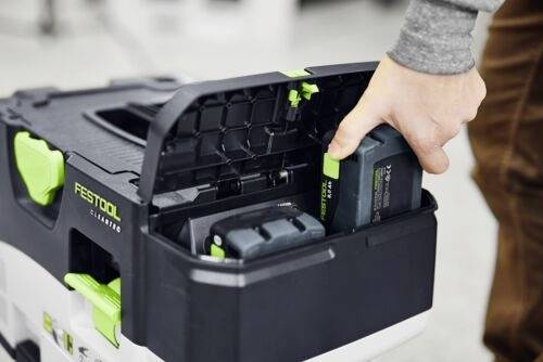 Osoba vkládá baterii do odsávače prachu Festool. Zařízení má černý a zelený design a obsahuje přihrádky pro nástroje.