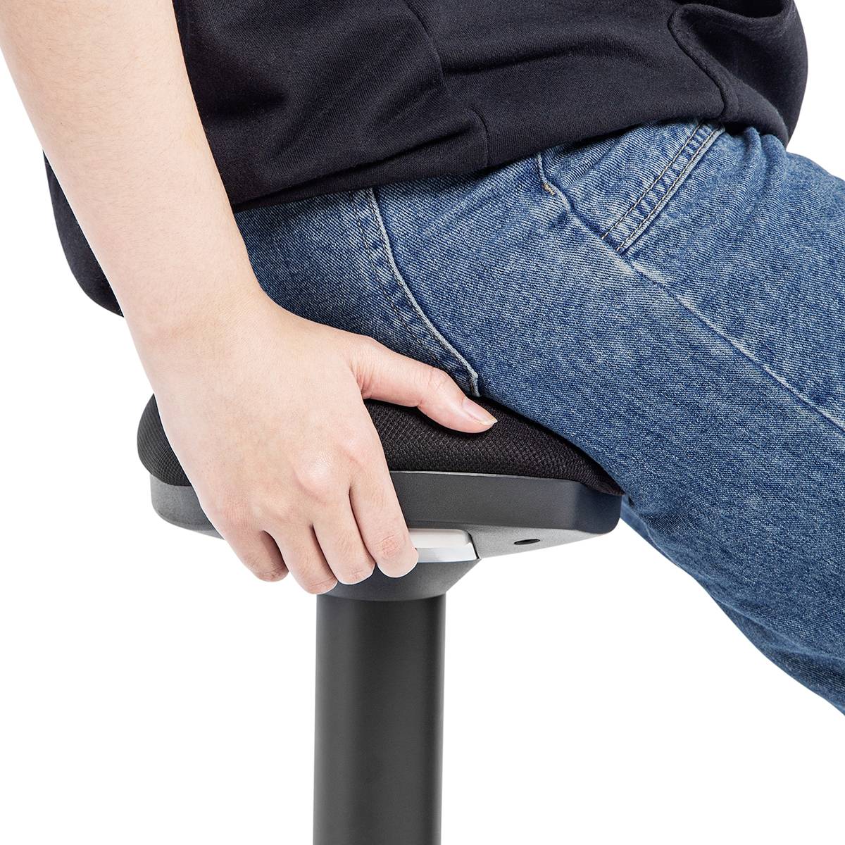 Osoba v džínách sedí na stoličce a nastavuje výšku sedadla pomocí páky, což ilustruje ergonomické úpravy sezení.
