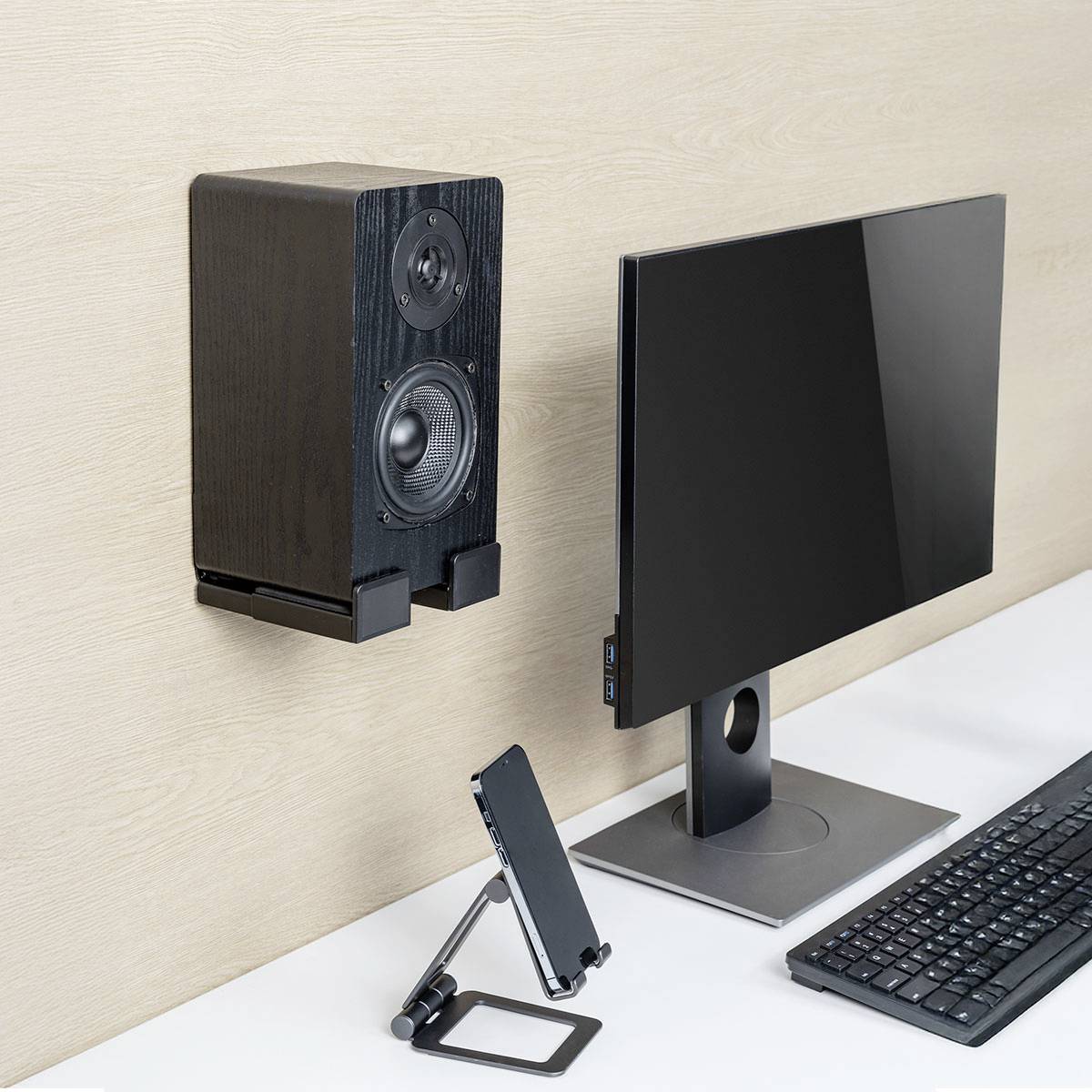 Stolní sestava s počítačovým monitorem a tabletem na stojanech vedle nástěnného reproduktoru. Minimalistický design v neutrálních barvách.