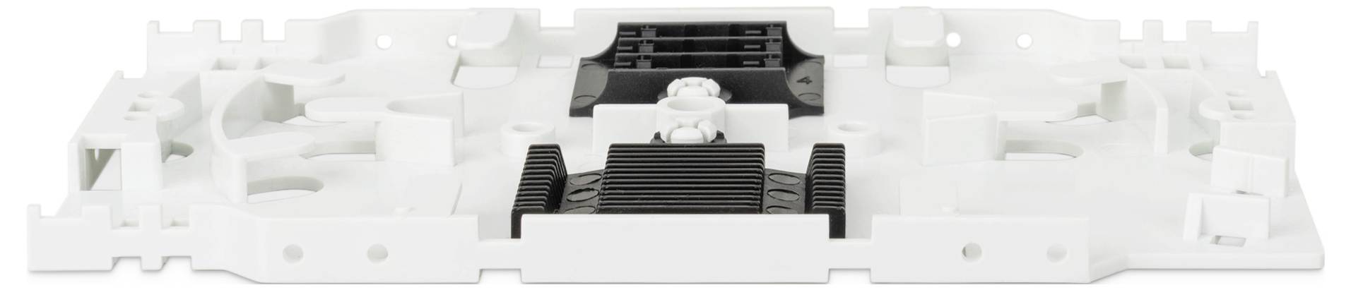 Bílá a černá plastová komponenta, pravděpodobně elektronický nebo mechanický díl, s různými drážkami, výstupky a montážními body.